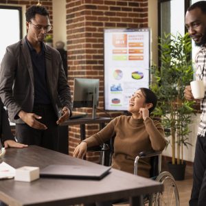 Multiracial professionals in a creative startup office taking a moment to unwind, chatting and laughing together during a break. African american man with glasses, sharing a story to his team.